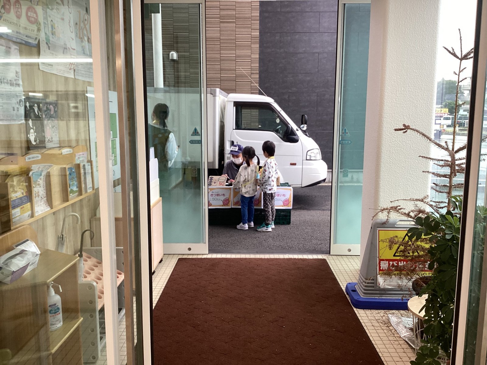 保育園の玄関先で、さつまいも売り場の前に立ちお芋を選ぶ2人の園児の後ろ姿